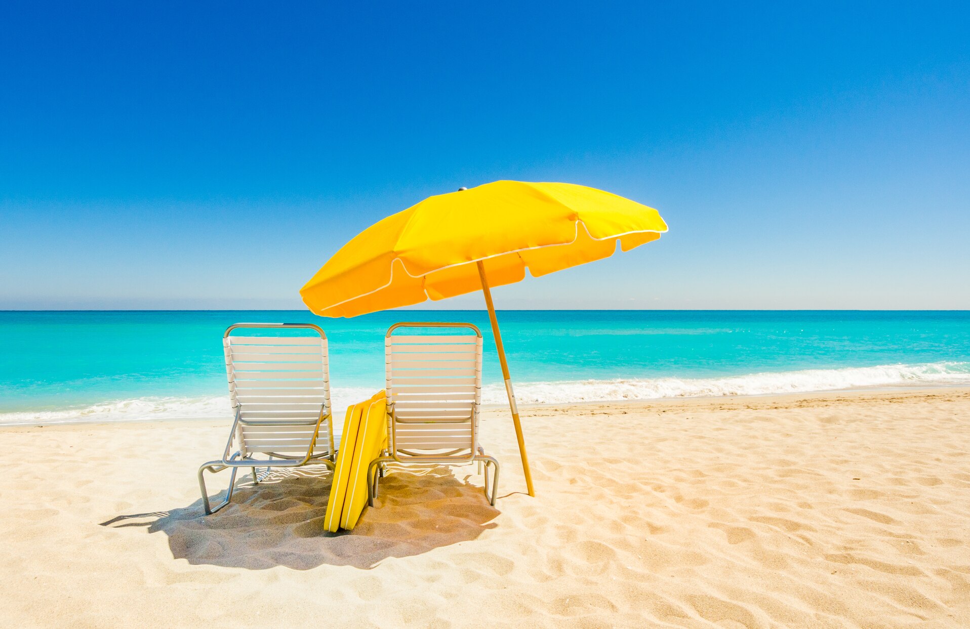 yellow umbrella and a white lounge chair on a beach