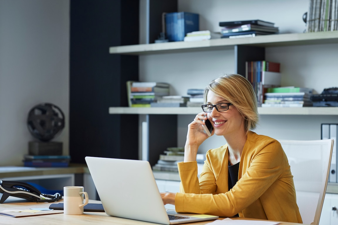 Woman talking on the phone while looking at her laptop.