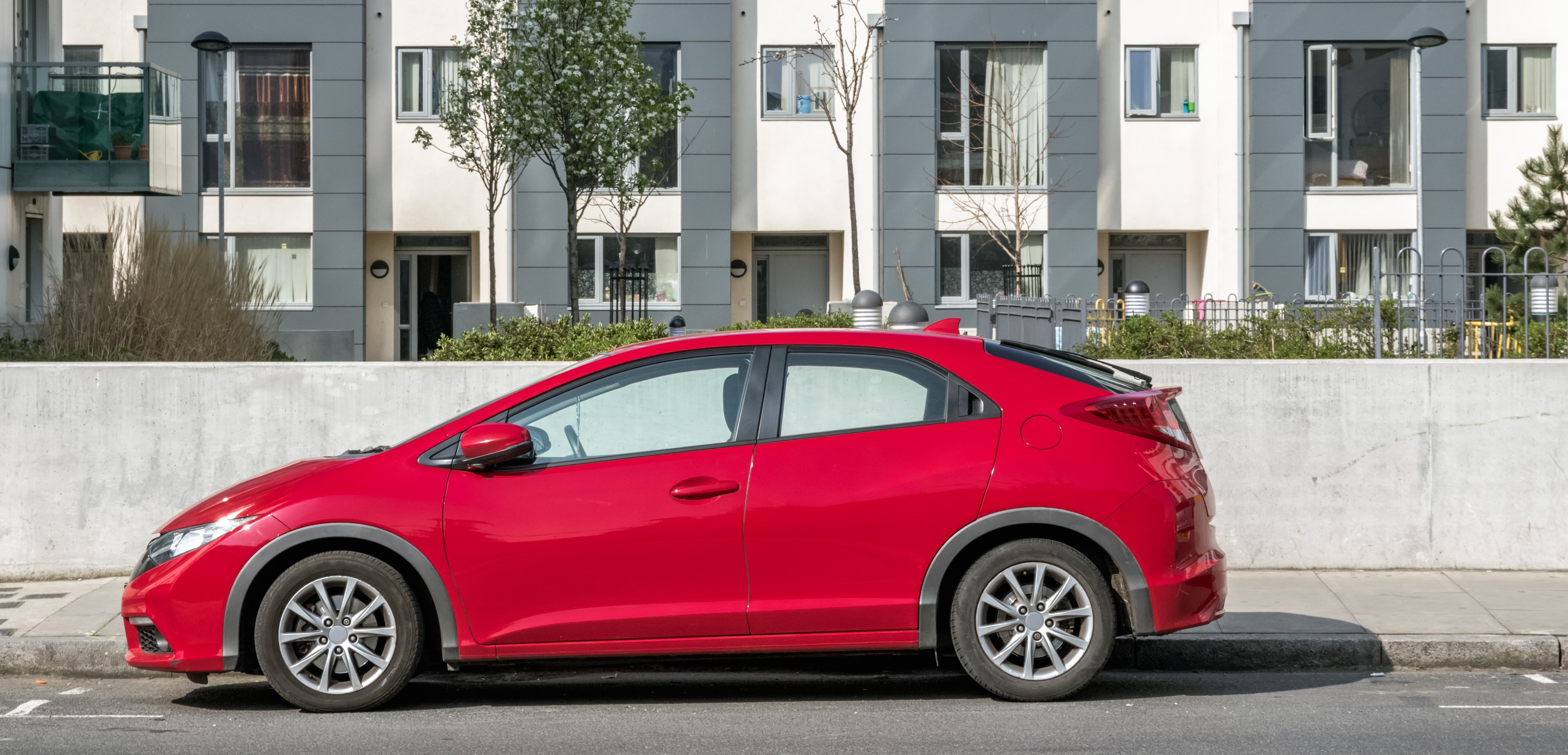 red hatchback car in front of apartment building