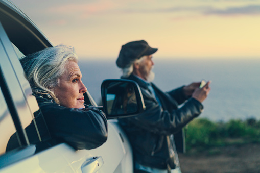 Woman looking out of car window, man standing outside of car taking photo