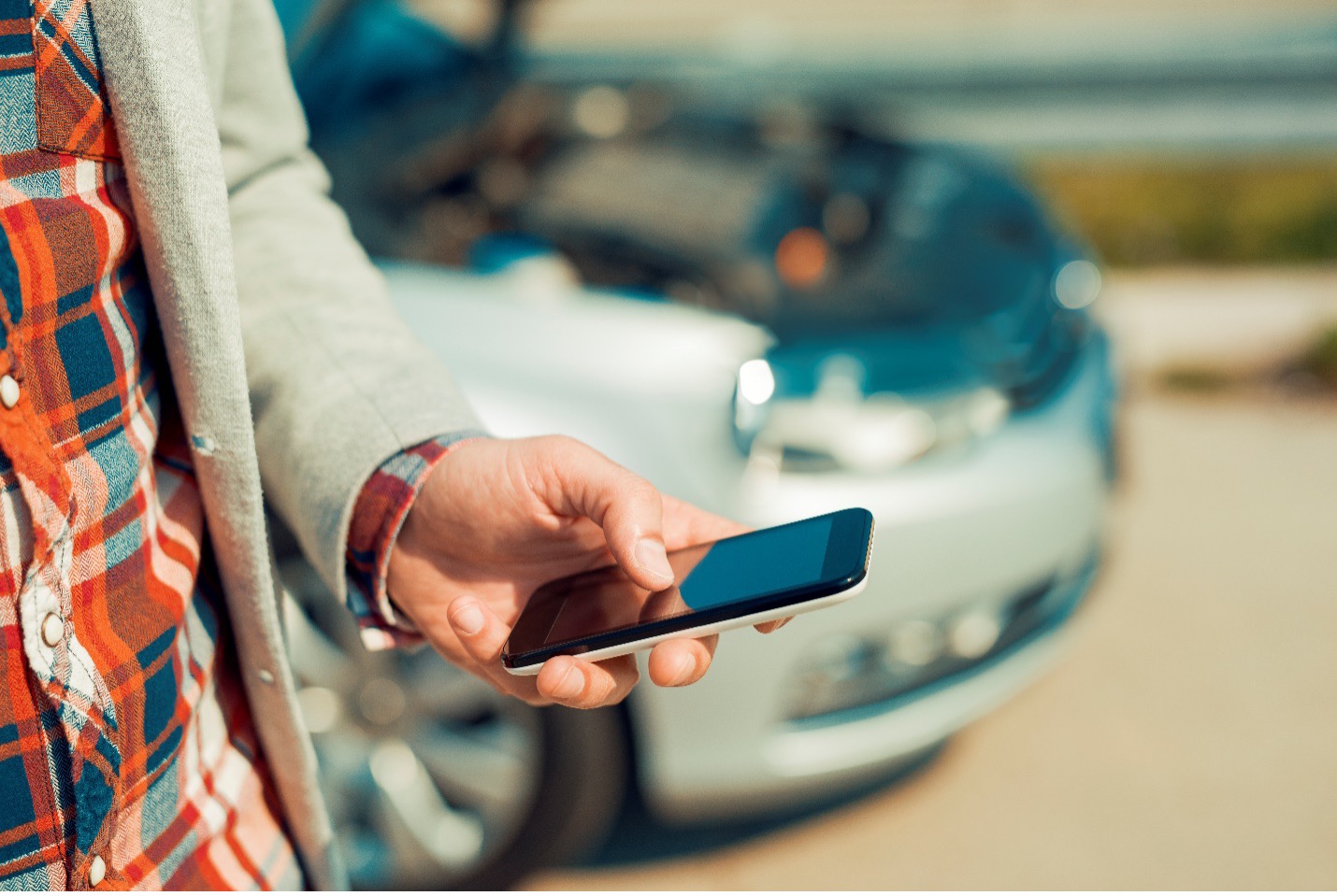 Person on phone in front of a car that has its hood up