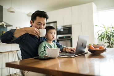 Man drinking coffee looking at laptop with his kid on his lap