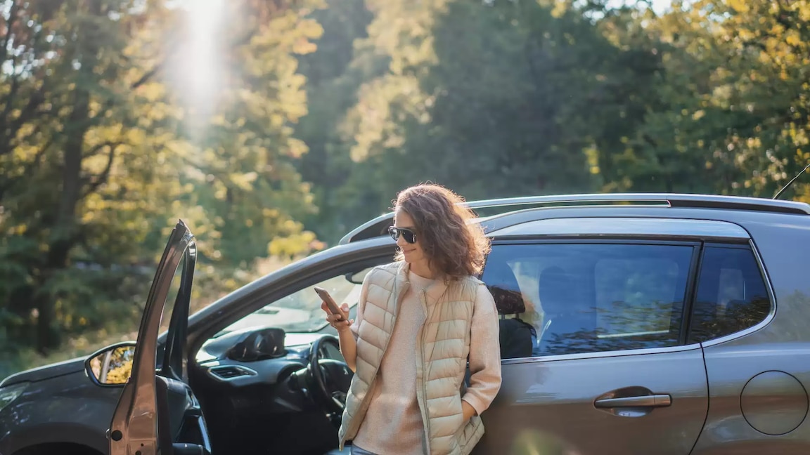 Woman standing next to car looking at phone