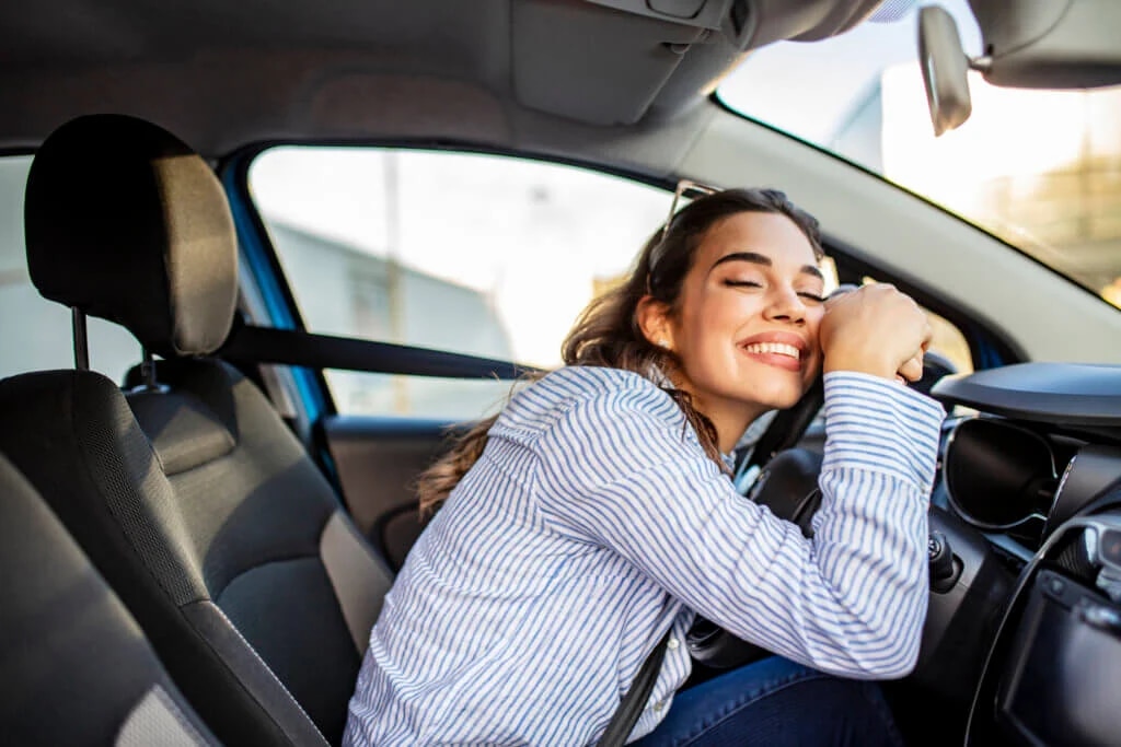 Woman sitting in a car laying on her steering wheel smiling