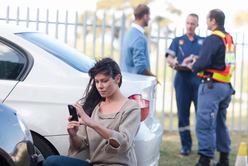 woman squating taking a picture with her cell phone of a minor car accident