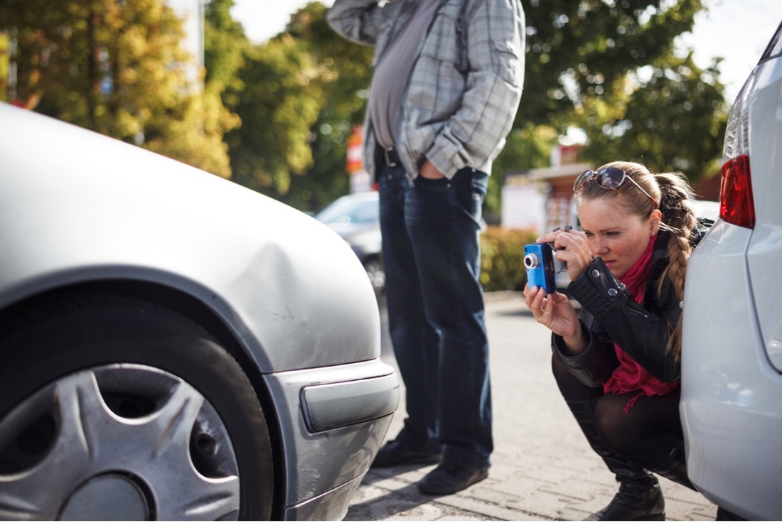 woman taking picture of damage to car after accident