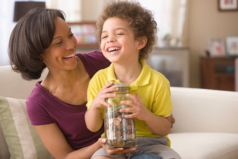 Woman and son laughing on the couch while son holds a jar of coins