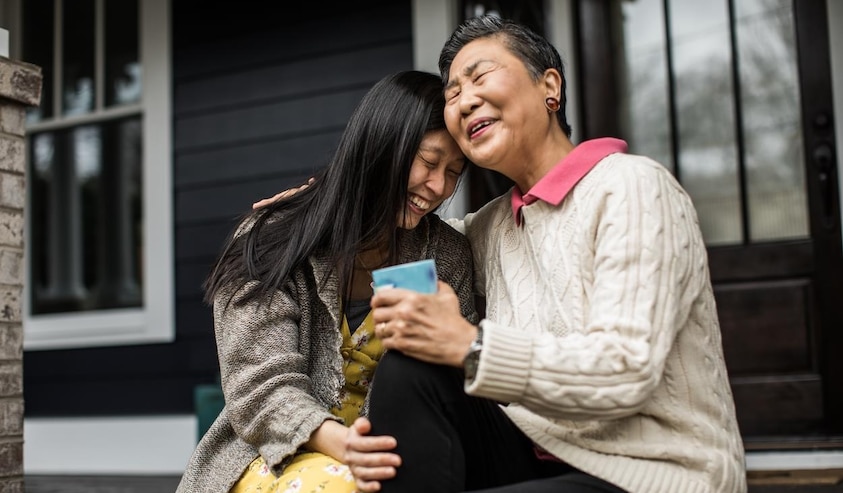 older mother and daughter laughing on porch