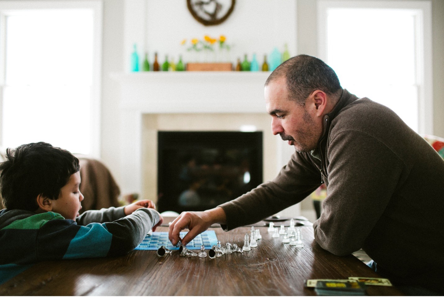 father and young son playing chess with glass chess set on table