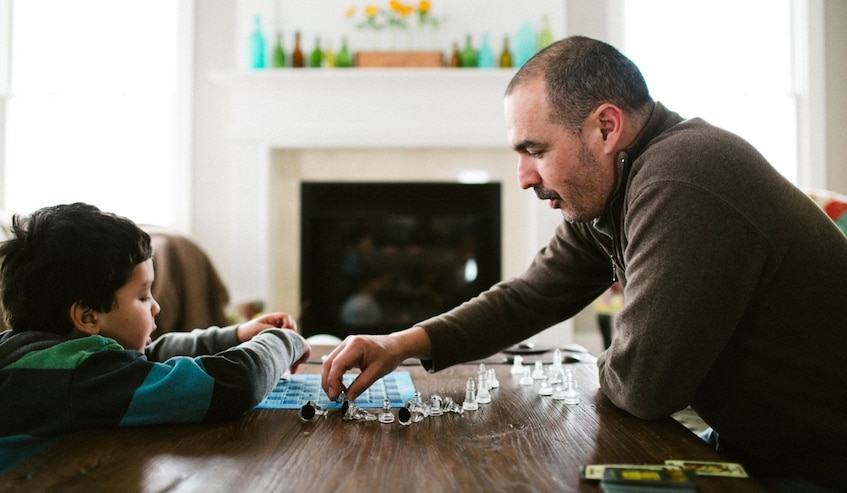 father and young son playing chess with glass chess set on table