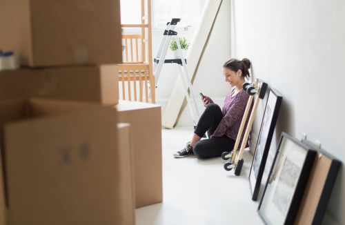 Woman sitting against a white wall while using her phone