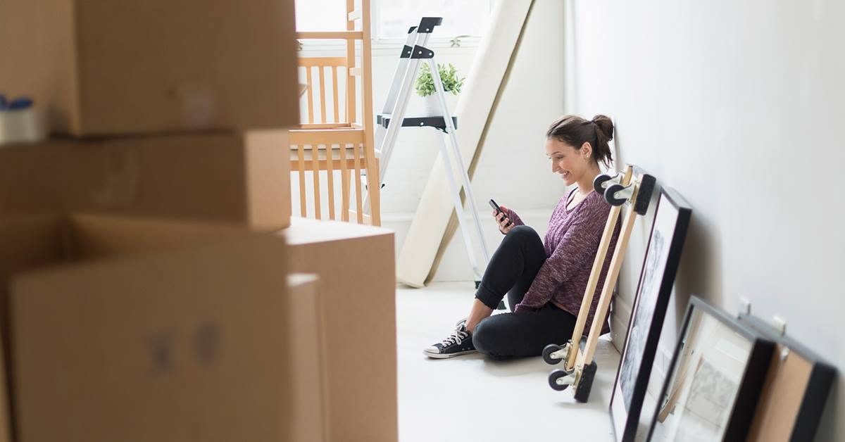Woman sitting against a white wall while using her phone