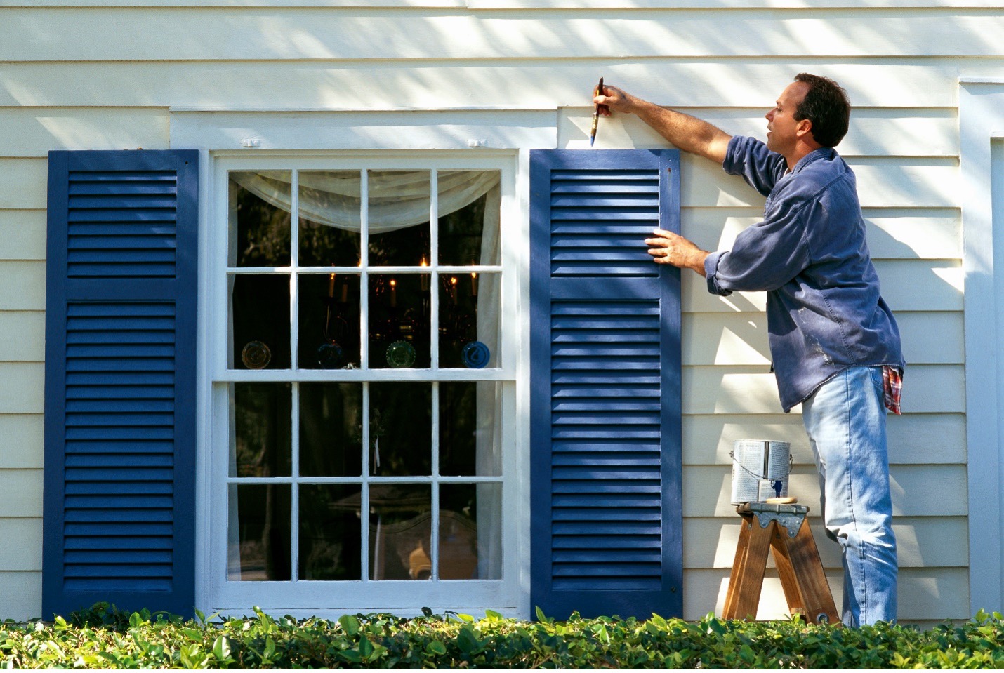 man on ladder painting shutters on the outside of house