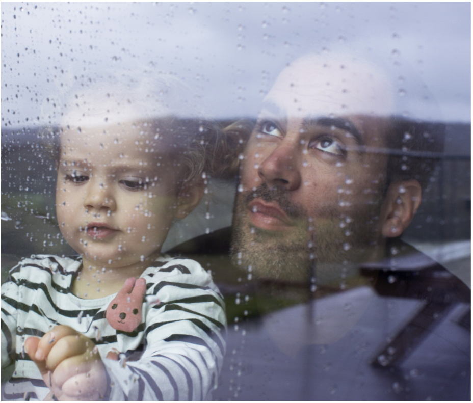 Father and child looking out of a wet window