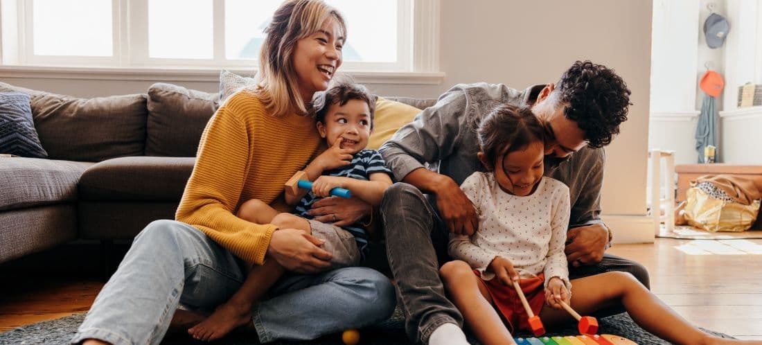 Parents sitting on the floor with their children in their living room playing with toys and smiling