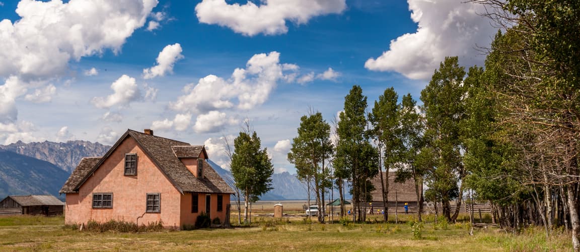 Small red house with brown roof on a large amount of land with a mountain range in the background