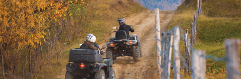 Two ATV riders ride a dirt path.