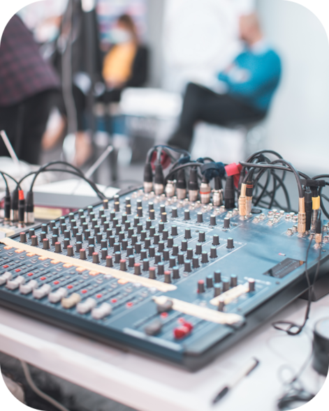 Audio mixing console with connected cables on a table, with blurred people in the background.