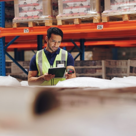 A man wearing a yellow reflective vest scanning boxes in a warehouse.