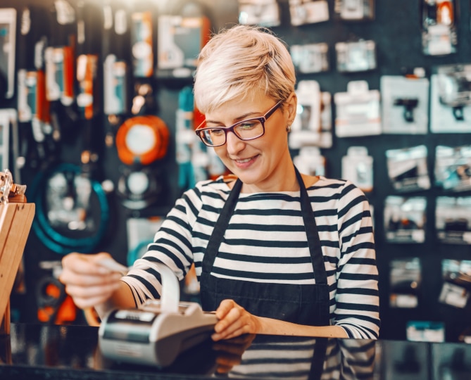 A woman standing at counter pulling tape out of credit card machine.