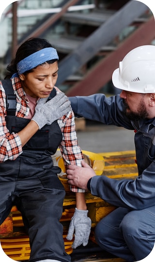 A woman holding her shoulder and a man in a white construction hat assisting her.