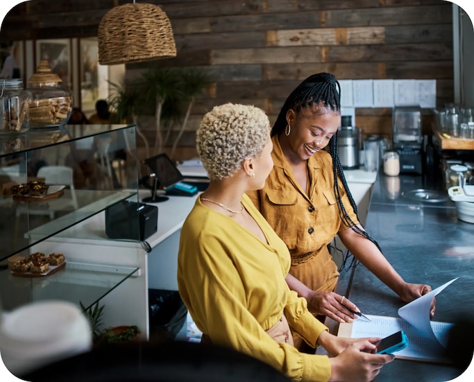 Two women standing behind a counter at a café looking at a clipboard.