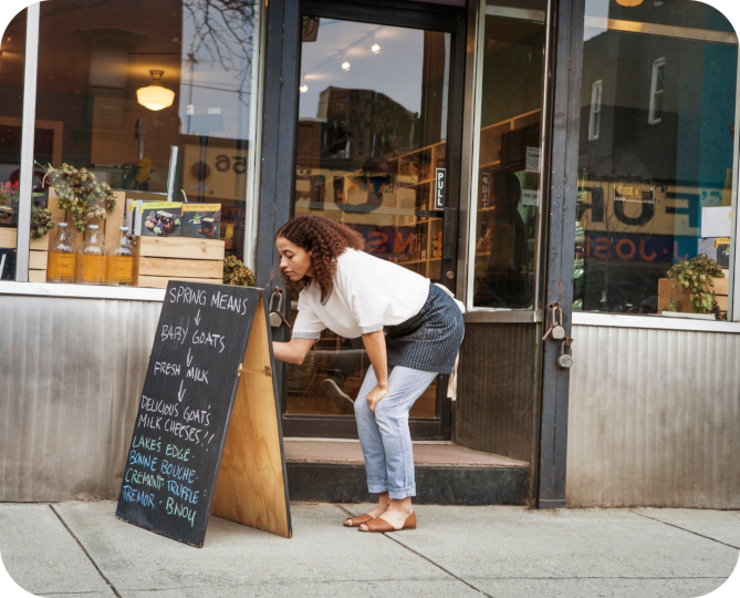 A woman writing on a chalkboard a-frame outside a shop.