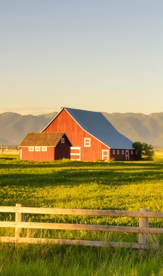 A red barn in middle of field with wood fence.