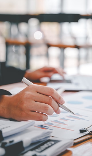 A hand holding a pen over a stack of papers.